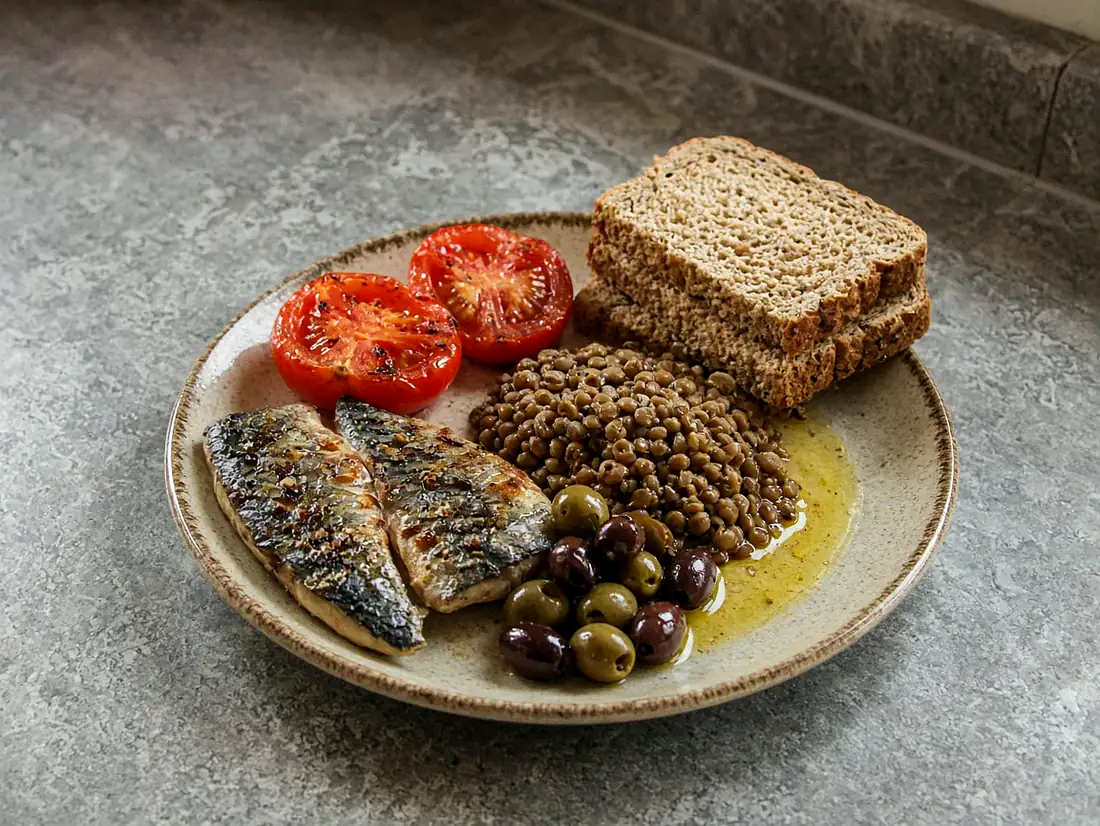 Gegrillte Makrele, Tomaten, Vollkornbrot, Linsen, Oliven und Olivenöl auf hellem Stein